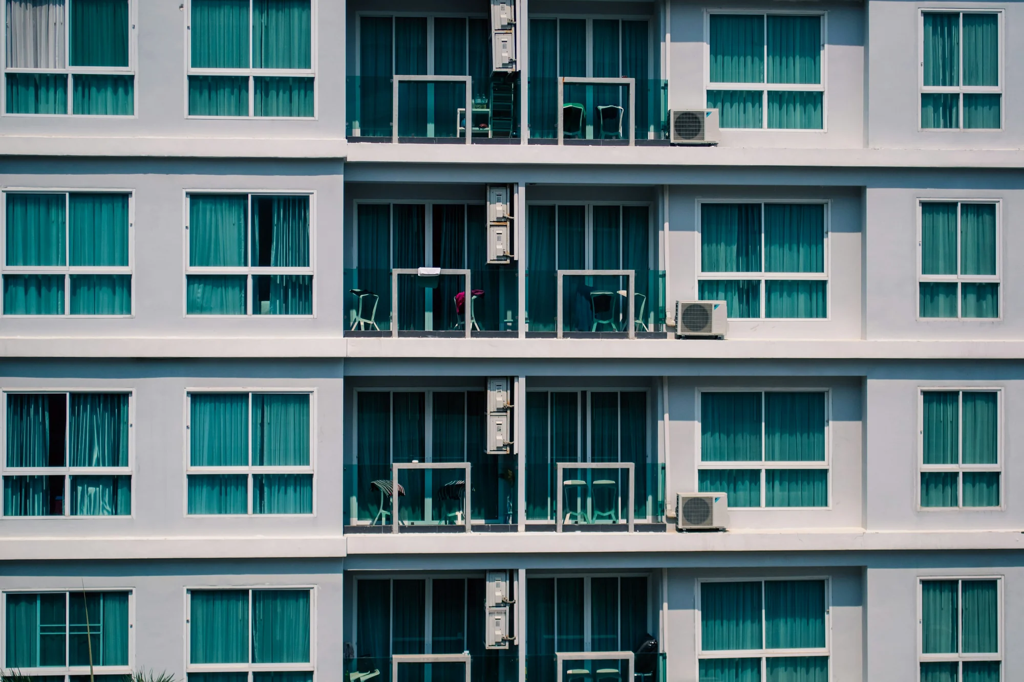 White residential facade with repeating balconies and turquoise curtains