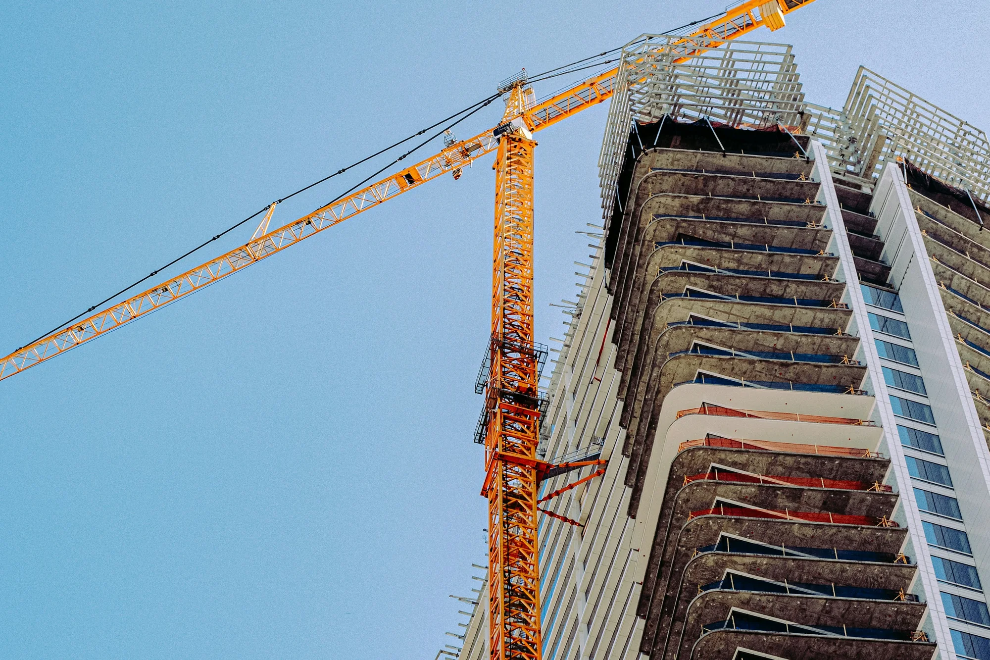 Orange construction crane beside an unfinished building under a blue sky
